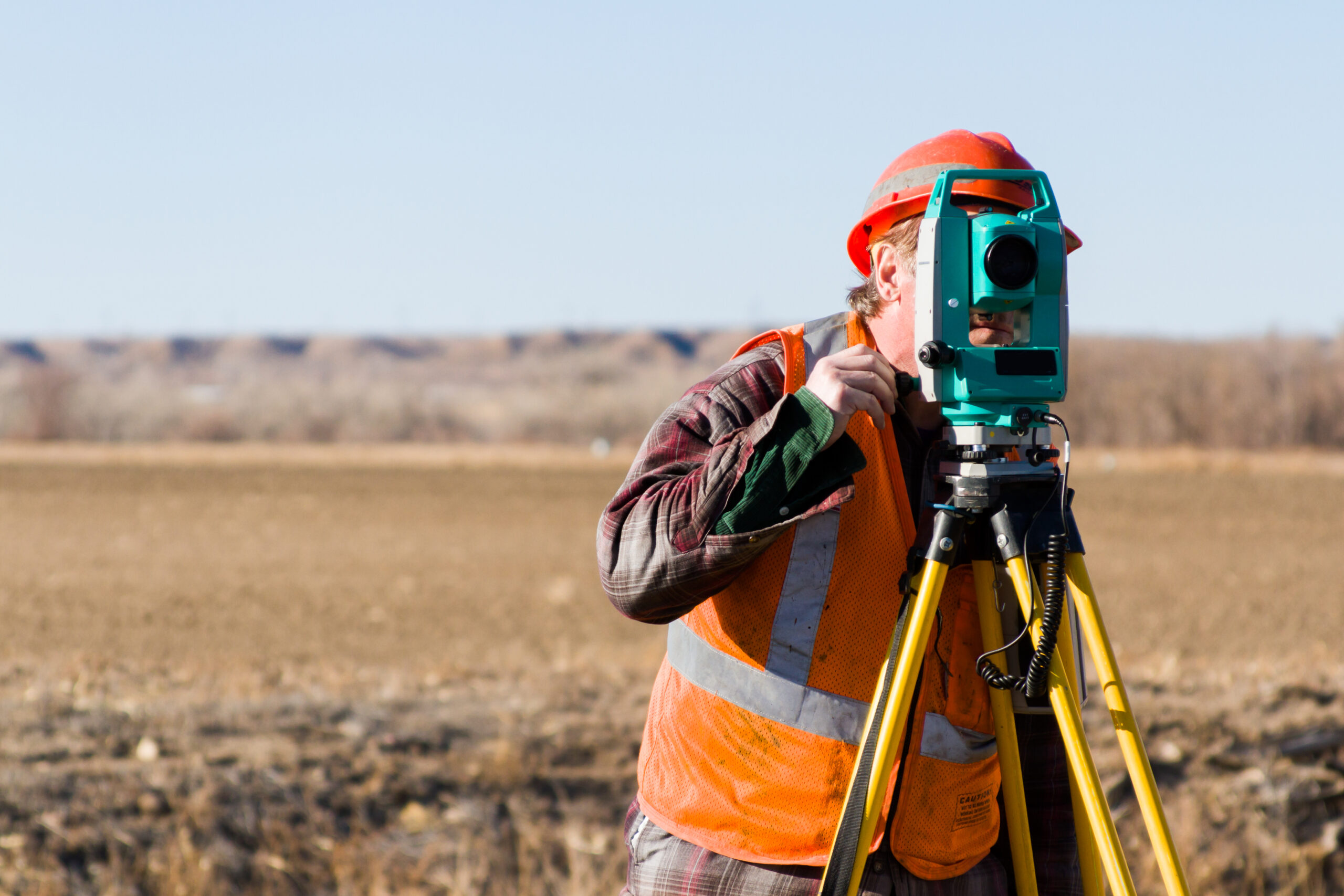 a man in orange vest and hard hat using a theodolite